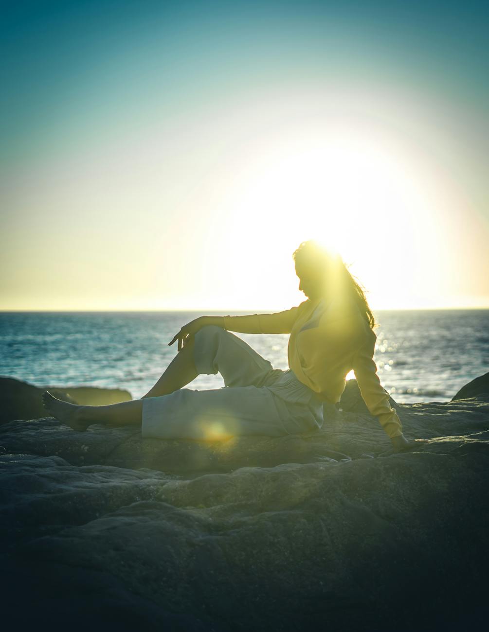 Person sitting cross-legged meditating by the ocean during sunrise